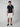 A man stands facing forward in a PROJEK RAW Mens Short Sleeve Knit Polo Sweater with white trim, paired with white shorts and navy slip-on shoes, set against a plain light background.