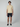 A young man stands facing forward in a light yellow PROJEK RAW Mens Short Sleeve Knit Polo Sweater, dark navy shorts, and black slip-on shoes against a plain light gray background.