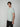 A young man with straight brown hair wears a pale grey PROJEK RAW Mens Short Sleeve Crew Neck T-shirt and black pants, standing against a plain light background, looking slightly to his left.