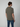 A young man with brown hair faces away from the camera, wearing a PROJEK RAW Mens Short Sleeve Carbon Peached Pigment Wash Jersey T-shirt and blue jeans against a neutral background for a subtle vintage vibe.