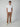 A man stands against a plain light background, wearing a white short-sleeved t-shirt, beige sneakers, and PROJEK RAW Mens 5-Pocket Regular Fit Denim in tan. He faces forward with a neutral expression and relaxed posture.