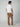 A man stands with his back to the camera, wearing a white short-sleeve t-shirt, PROJEK RAW Mens 5-Pocket Regular Fit Denim in brown, and white sneakers against a plain light background.
