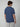 A person with brown hair is seen from the back, wearing a PROJEK RAW Mens Short Sleeve Graphic T-Shirt and light gray pants, set against a plain light background.