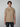 A young man with short brown hair wears a beige PROJEK RAW Mens Short Sleeve Graphic T-Shirt with a front pocket and faded lettering, standing against a light gray background and looking at the camera.