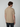A man with brown hair, seen from behind, wears a beige PROJEK RAW Mens Short Sleeve Graphic T-Shirt and dark jeans against a plain light gray background.