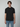 A young man with short brown hair wears a PROJEK RAW Mens Short Sleeve Carbon Peached Pigment Wash Jersey T-shirt and blue jeans, standing facing forward against a plain light gray background.