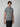 A young man with brown hair wears a PROJEK RAW Mens Short Sleeve Marled Jersey Polo and black pants, standing against a plain light gray background. A small black graphic details the lower left side of his polo shirt.