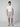 A man faces forward wearing a plain white t-shirt, tailored fit light gray PROJEK RAW MENS CHINO SHORT, and gray sneakers against a neutral light gray background.