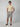 A man stands with hands in his pockets against a light gray background, wearing PROJEK RAW MENS PLEATED DRAWSTRING CHINO SHORTS, a yellow polo shirt, sunglasses, and brown sandals—showcasing effortless summer style.