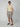 A man wearing sunglasses, a light yellow short-sleeve polo, and PROJEK RAW MENS PLEATED DRAWSTRING CHINO SHORT stands against a plain light gray background, embodying effortless summer style with brown sandals.