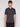 A young man with medium-length brown hair wears the Projek Raw AARON-CHARCOAL short-sleeve polo shirt and black pants, standing against a plain white background, facing forward with a neutral expression.