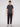 A person stands facing forward against a plain white background, wearing the Projek Raw AARON-CHARCOAL short-sleeve polo shirt, black pants, and white sneakers.