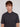 A young man with light brown hair and blue eyes wears the Projek Raw AARON-CHARCOAL short-sleeve polo, standing against a plain white background and looking directly at the camera with a neutral expression.