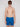 A young man models Projek Raw’s BRYSON-BLUE swim trunks and black sunglasses, standing against a plain light background with a neutral expression.