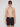 A young man stands against a plain light background, facing forward with a neutral expression, wearing Projek Raw’s BRUNO-CHARCOAL swim trunks and black sunglasses.
