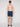 A man faces forward against a white background, wearing Projek Raw BRUNO-NAVY swim shorts featuring a palm tree pattern, paired with black sunglasses and slide sandals. He is shirtless and maintains a neutral expression.