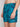 A person wears Projek Raws BRUNO-TURQUOISE swim trunks, featuring a blue palm tree pattern and a drawstring waistband, shown from mid-torso to thigh against a plain background.