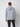 A man faces away from the camera wearing the PROJEK RAW Mens Long Sleeve Hoodie with Kangaroo Pocket in light gray and black pants, set against a plain white background.