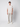A young man with short curly hair stands against a white background, wearing a light beige t-shirt, PROJEK RAW Men’s Relaxed Chino Pant, and white sneakers. His expression is neutral.