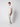 A young man with curly hair stands sideways against a plain white background, wearing a light beige t-shirt, PROJEK RAW Men’s Relaxed Chino Pant, and white platform sneakers.