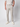 A person stands against a plain background with one hand in their pocket, wearing a white short-sleeve shirt, PROJEK RAW Men’s Relaxed Chino Pant in light grey, and white sneakers.
