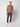 A young man stands against a plain background, wearing PROJEK RAW Men’s Textured Bungee Pull-on Chino Pant in dark gray, a light brown quarter-zip sweater, and white sneakers. He looks at the camera with a neutral expression and relaxed posture.