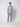 A young man faces forward against a plain light gray background, wearing a light gray turtleneck sweater, PROJEK RAW Men’s Bungee Trouser, and white sneakers.