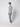 A young man with curly hair stands sideways against a plain light background, wearing a gray turtleneck sweater, PROJEK RAW Men’s Bungee Trouser, and white sneakers.