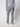 A person stands facing away, wearing a light gray long-sleeve top, PROJEK RAW Men’s Bungee Trouser in stretch fabric, and white sneakers against a plain light background.