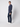 A man stands sideways against a plain background, wearing PROJEK RAW Mens 5-Pocket Flex Knit Jeans in navy blue, a matching navy sweater, and white sneakers. He faces the camera with a neutral expression.