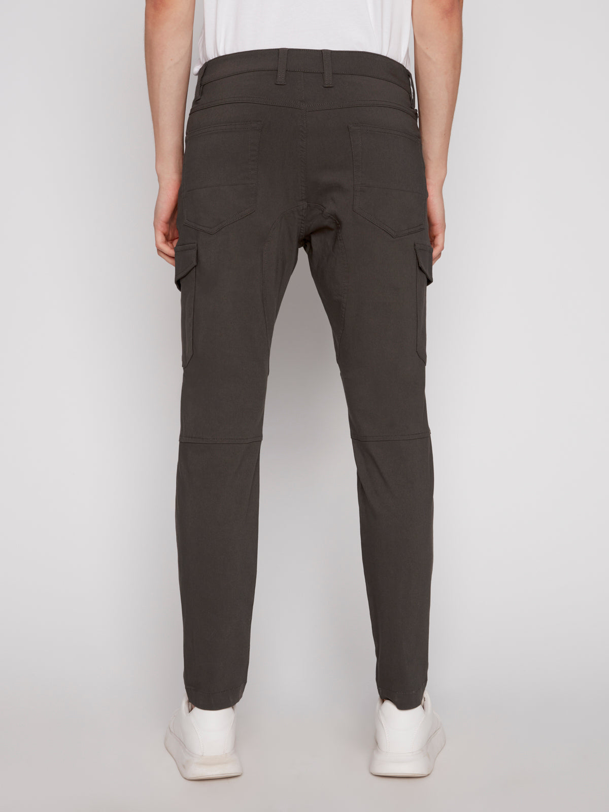 A person is seen from the back against a plain light background, wearing olive green Projek Raw STEPHANE-OLIVE cargo pants and white sneakers.
