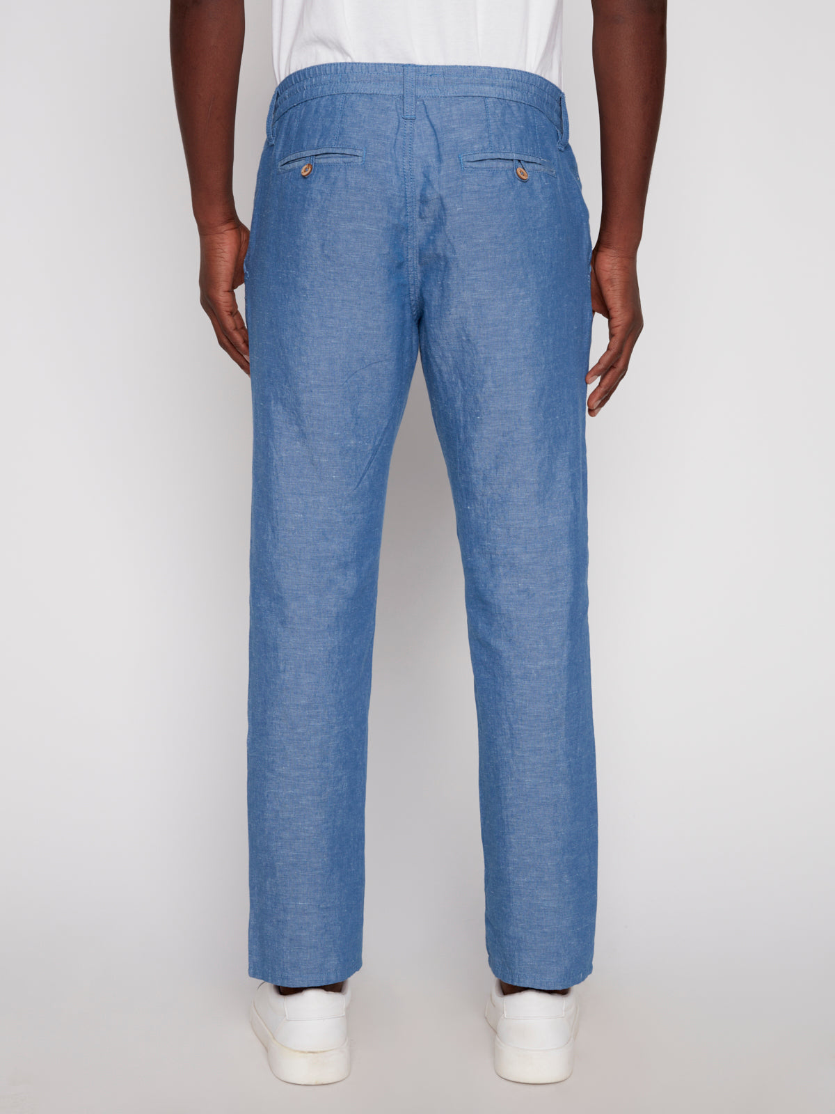 A person wears Projek Raw’s LUC-BLUE light blue dress pants with buttoned back pockets and white sneakers, viewed from the back against a plain background—ideal summer style.