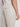 A person is seen from the side wearing Projek Raws LUC-NATURAL linen drawstring pants and a white shirt, highlighting the elastic waistband, detailed seams, and back pocket with button.