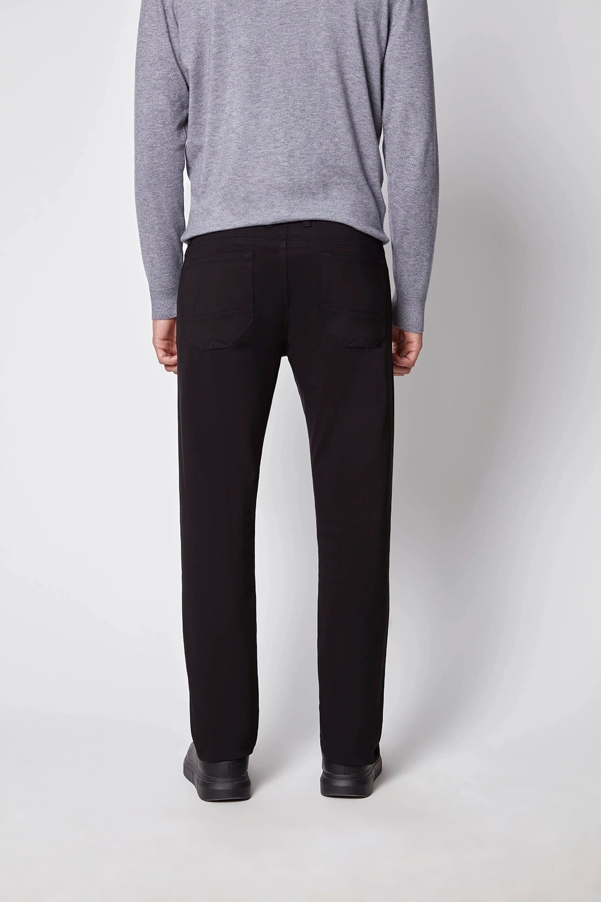A person stands facing away in a light gray long-sleeve sweater, PROJEK RAW Mens 5-pocket Classic Stretch Bungee Pants, and black shoes, set against a plain light background.