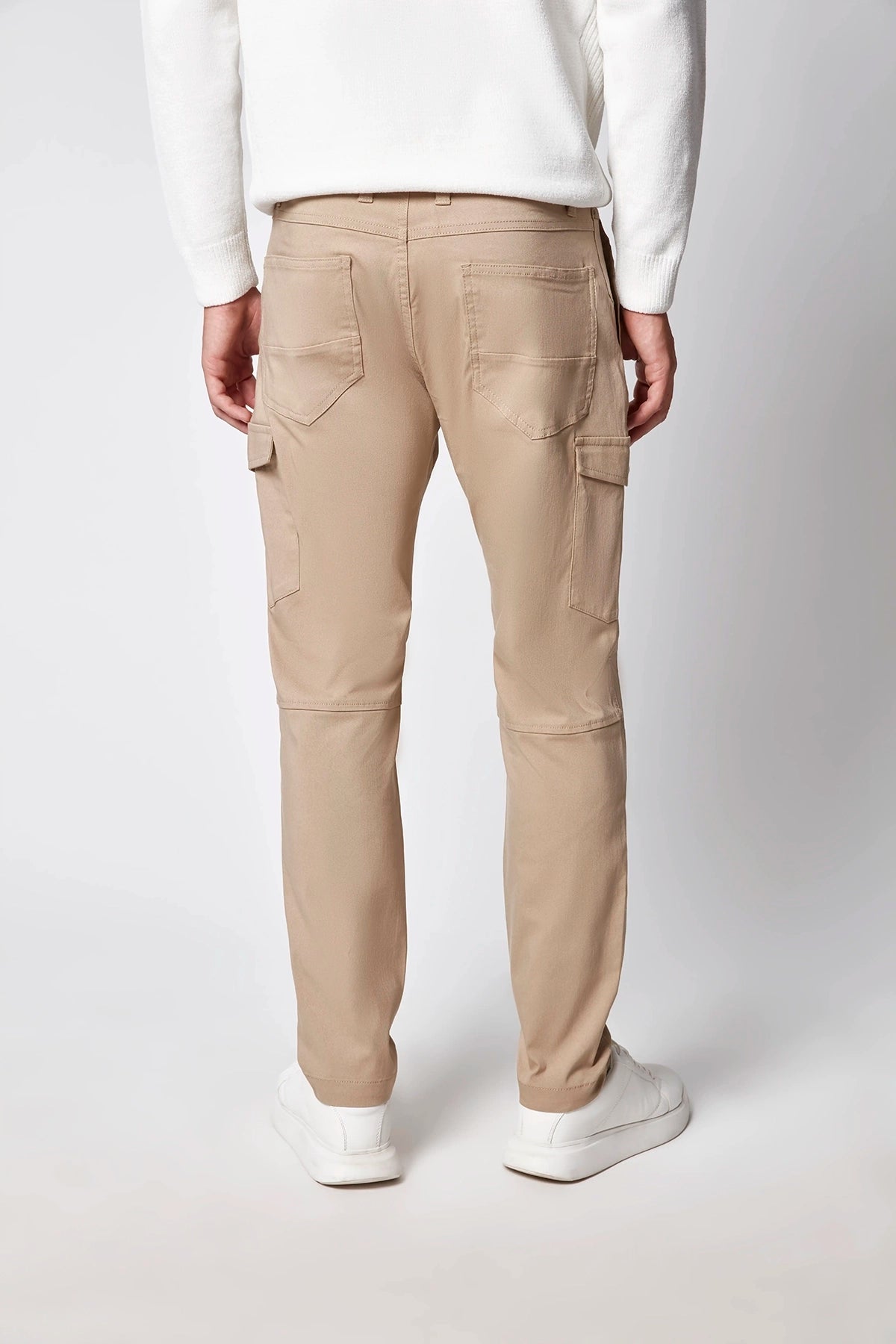 A person wearing PROJEK RAW Mens Stretch Bungee Cargo Pant in beige, paired with a white sweater and white sneakers, stands with their back to the camera against a plain light background.