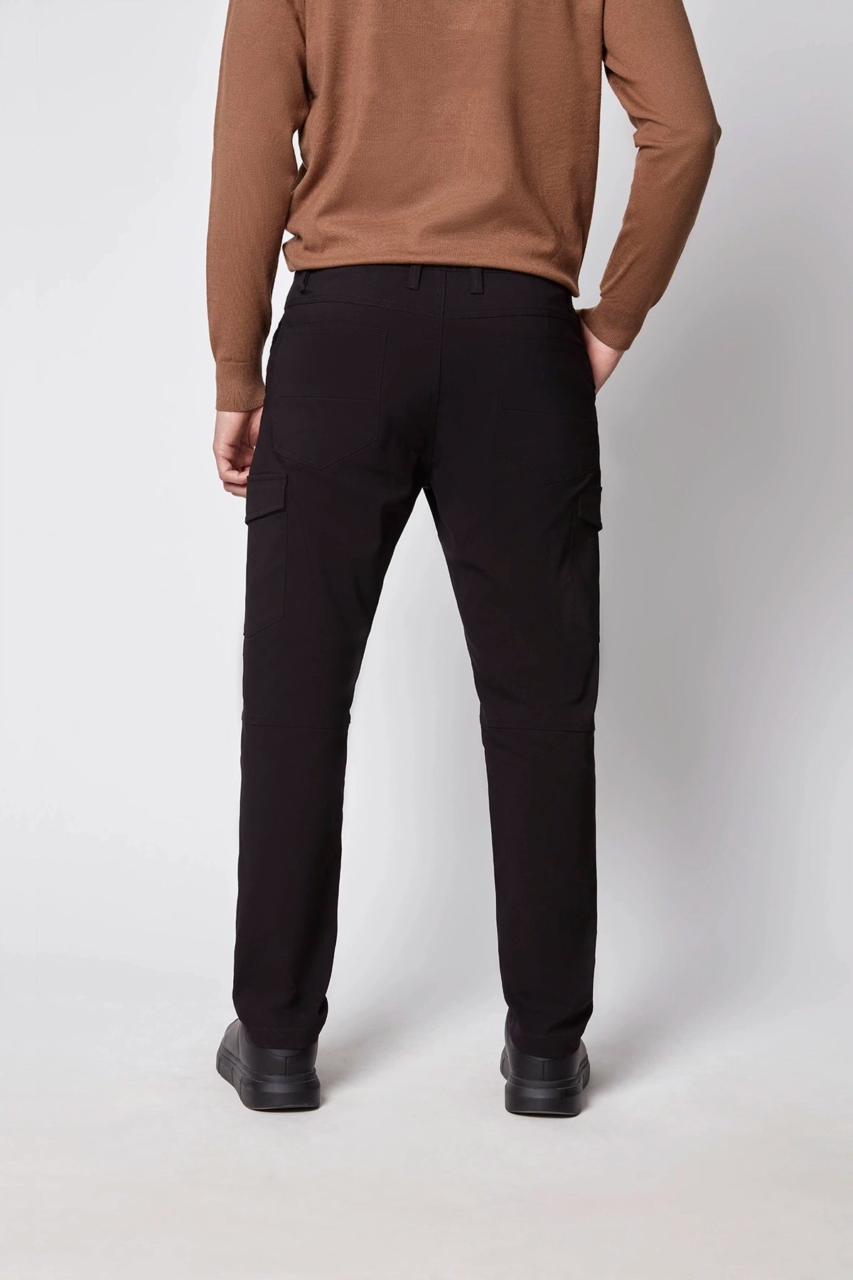 A person stands facing away in a brown long-sleeve top, black PROJEK RAW Mens Stretch Bungee Cargo Pant, and black shoes against a plain light background.