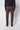 A person wearing PROJEK RAW Mens Stretch Bungee Cargo Pant in dark brown, paired with a black long-sleeve top and black shoes, stands facing away from the camera against a plain light gray background.