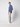A young man stands sideways against a plain light gray background, wearing PROJEK RAW Mens Bungee Relaxed Chino Pant in light gray, paired with a blue button-up shirt and white sneakers.