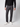 A person stands against a plain light background, shown from shoulders down, wearing PROJEK RAW Men’s Brushed Bungee 5-Pocket Pants in dark gray, a black long-sleeve top, and white sneakers.