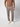 A person wearing a brown long-sleeve top, PROJEK RAW Men’s Houndstooth Bungee Tailored Pant, and white sneakers stands with one hand in their pocket against a plain light background.