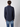 A man with curly brown hair stands facing away, wearing a PROJEK RAW Mens Long Sleeve Casual Dress Shirt and light blue jeans against a plain light background.