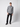 A man stands against a plain light background, wearing a gray plaid shirt, black PROJEK RAW Mens 5-Pocket Straight Fit Jeans, and black shoes. He faces the camera with a neutral expression, one hand by his side.