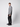 A man stands sideways against a plain light background, wearing a gray plaid button-up shirt, black sneakers, and PROJEK RAW Mens 5-Pocket Straight Fit Jeans.