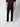 A person in a short-sleeve black shirt, PROJEK RAW Mens 5-Pocket Straight Fit Jean in black rinse, and white sneakers stands against a plain light background with hands relaxed at their sides.