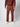 A person, head not visible, stands against a plain background wearing PROJEK RAW Mens Colored Denim Carpenter Pants in rust with a matching ribbed sweater and white sneakers.
