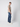 A young man stands sideways against a white background, wearing a beige t-shirt, PROJEK RAW Mens 5-Pocket Straight Fit Jeans, and white sneakers, looking toward the camera.