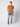 A man stands against a plain light background wearing a PROJEK RAW Mens Short Sleeve Crewneck T-shirt in brown, paired with blue jeans and white sneakers, one hand in his pocket and a neutral expression.