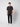 A young man stands against a plain light gray background, wearing a dark short-sleeve shirt, PROJEK RAW Mens 5-Pocket Straight Fit Jean in black rinse, and white sneakers. He looks straight ahead with a neutral expression.