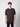 A young man with curly brown hair wears the PROJEK RAW Mens Short Sleeve Crew T-shirt and black pants, standing against a plain light gray background, looking straight at the camera with a neutral expression.
