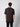 A man with short, curly brown hair faces away from the camera, wearing a PROJEK RAW Mens Short Sleeve Crew T-shirt and black pants against a plain light gray background.
